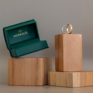 Argollas de matrimonio en oro junto a estuche verde MONOCH sobre bases de madera